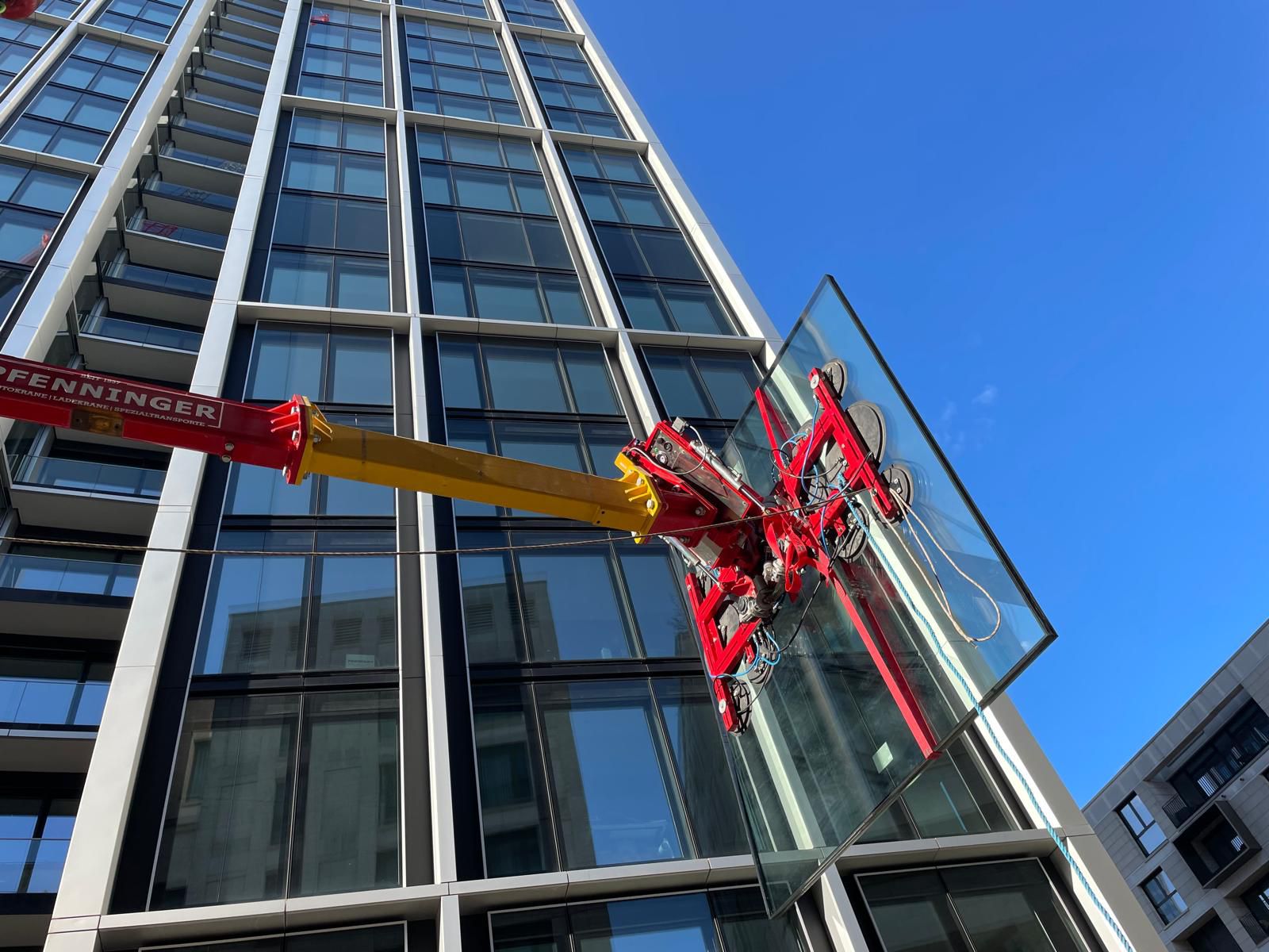 Glasmontagegerät hält große Glasscheibe an moderner Gebäudefassade.